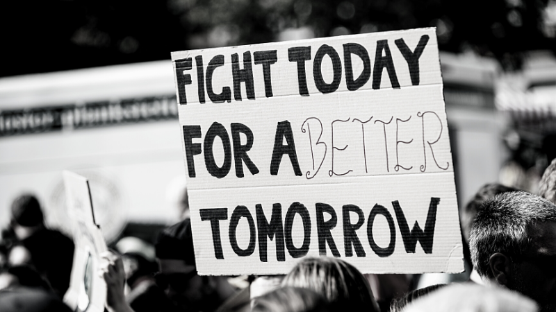 Image of a protester holding a sign reading "fight today for a better tomorrow"