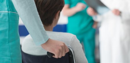 Nurse guides patient in wheelchair toward group of medical professionals